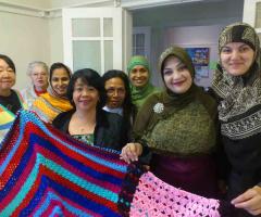 Group of women from different cultural backgrounds and different ages holding up crocheted rugs