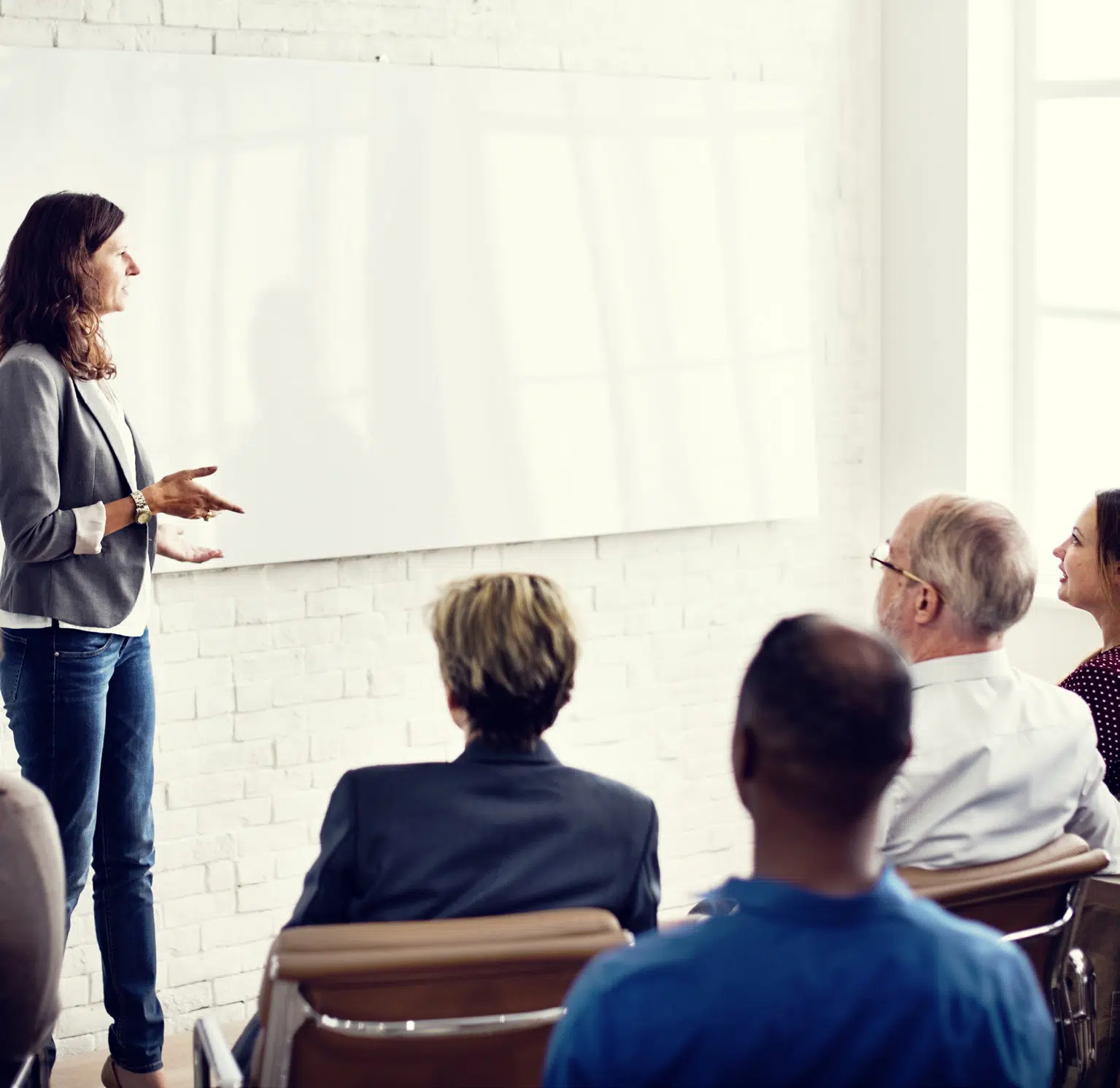 Woman standing at the front of a classroom, speaking to a seated group of adult students.