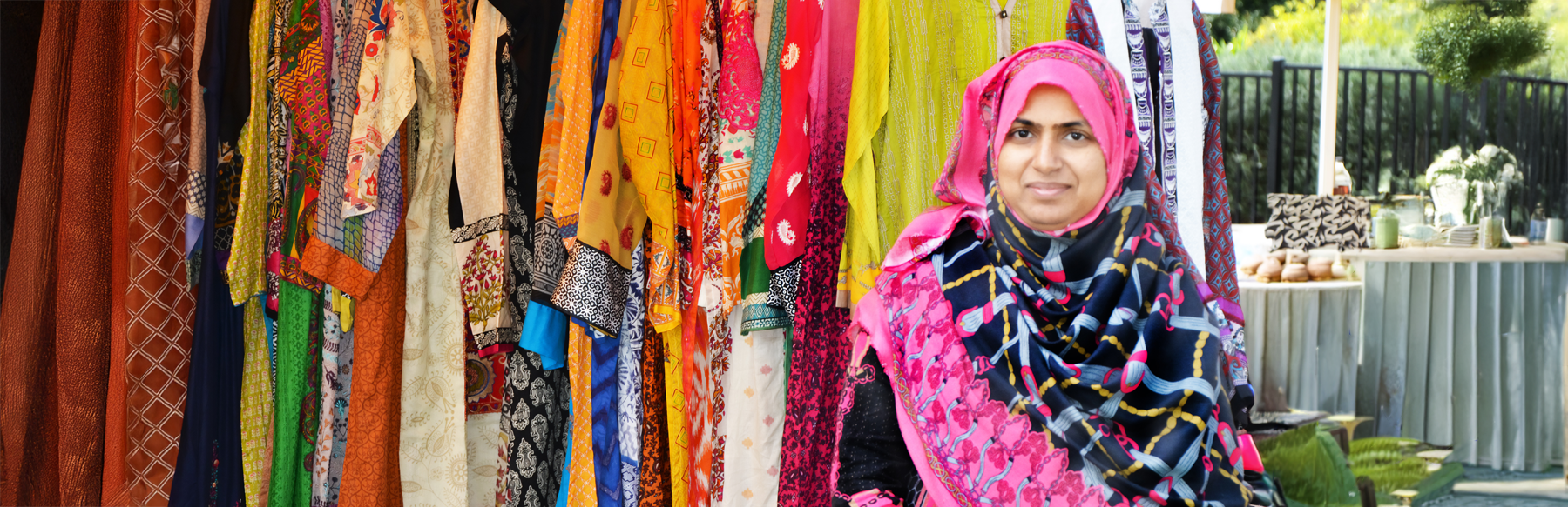 A woman is sitting under a tent with a colourful display of clothing